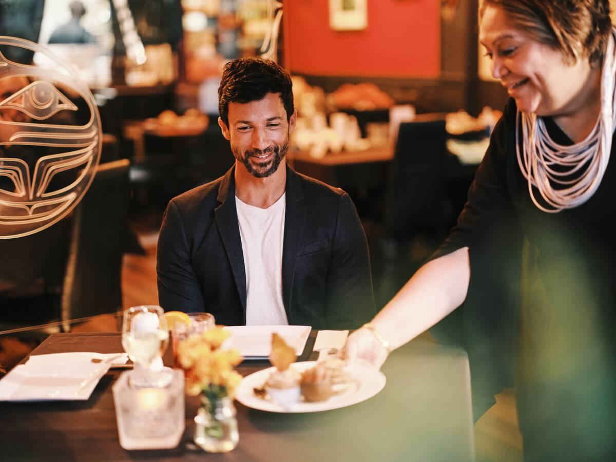 Inez Cook, the owner of Salmon N
Bannock in Vancouver, serves food to a couple
at the restaurant.