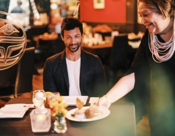 Inez Cook, the owner of Salmon N
Bannock in Vancouver, serves food to a couple
at the restaurant.